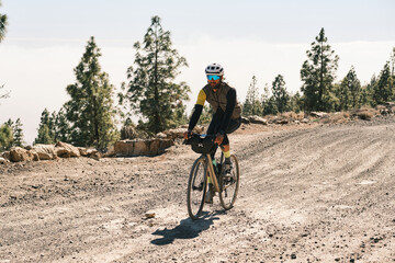 Fototapeta premium A cyclist enjoys a scenic gravel road ride through a pine forest. Sunlight illuminates the trail and the cyclist's journey. Perfect for adventure, travel, and outdoor lifestyle imagery.