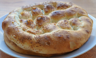 Freshly baked round ramadan pide bread with sesame seeds on white plate on wooden table