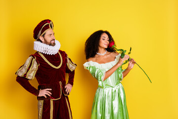 Elegant couple in historical costumes enjoying a playful moment with a vibrant yellow background