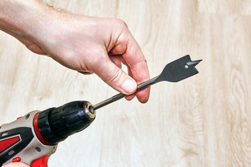 Cordless drill with spade bit held by hand.