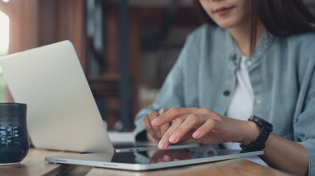 Business woman using digital tablet and working on laptop computer on wooden table at coffee shop. Student studying online, searching the information, surfing the internet at cafe - Powered by Adobe