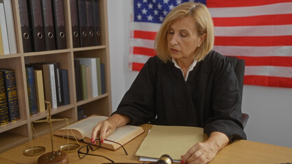 Mature woman judge in an american courtroom reading documents with an open book wearing a black robe and sitting in front of the united states flag