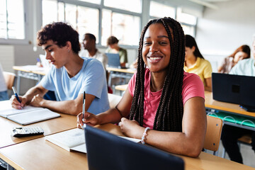 Portrait of smiling female student looking at camera while studying in class. Diverse young teenage people learning in the school
