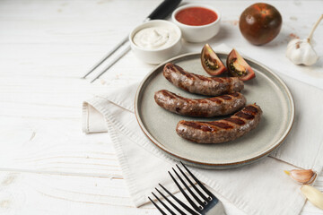 Ready to eat grilled sausages on the plate, white wooden background, close up