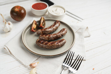 Ready to eat grilled sausages on the plate, white wooden background, close up
