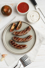 Ready to eat grilled sausages on the plate, white wooden background, close up