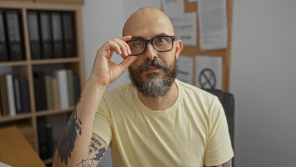 Handsome hispanic man with a beard and glasses sitting in an office workspace looking into the...