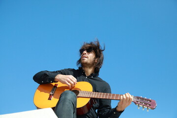 Obraz premium Young Long Hair Man Plays Classical Guitar Outside, Low Angle