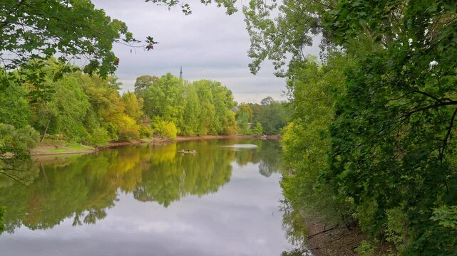Calm mirror reflection on a lake surrounded by colorful trees changing color on an overcast fall day 