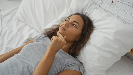 Young woman lying in bed thinking in a bright bedroom with a white pillow