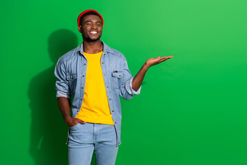 Stylish young man in denim outfit and beanie presenting on green background, demonstrating casual fashion and positive lifestyle
