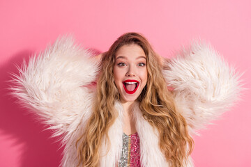 Happy woman in a glamorous fur coat on pink background showing excitement with open smile and...