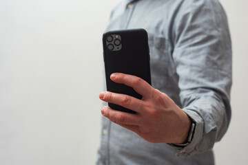 Close-up of a man wearing a gray shirt, holding a smartphone in hand as if taking a photo or...
