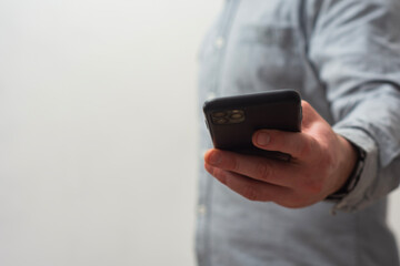 Close-up of a man wearing a gray shirt, holding a smartphone in hand as if taking a photo or recording a video.