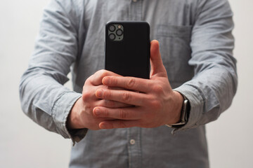 Close-up of a man wearing a gray shirt, holding a smartphone with both hands as if taking a photo or recording a video.