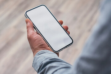 Person holding mockup smartphone with blank screen against the wooden floor.