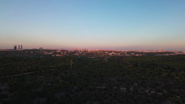 Camera ascends over Madrid&rsquo;s Casa de Campo during golden hour, revealing vast canopy of lush trees. In the distance, the city's skyline glows under the warm evening sunlight, creating a stunning view.