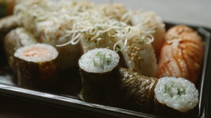 Close-up of various sushi rolls and sashimi on a black tray placed on a concrete surface