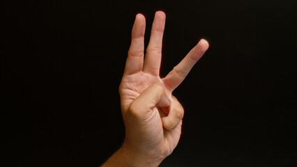 Man's hand showing the number three gesture on a dark background