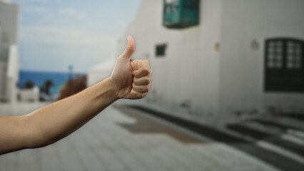 Man displaying thumb up gesture with focus on hand against blurred outdoor urban backdrop on a...
