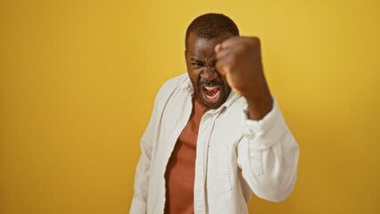 Man showing fist gesture over isolated yellow background, conveying powerful emotion and excitement...