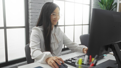 Woman working at computer in modern office with natural light, focused and professional atmosphere,...