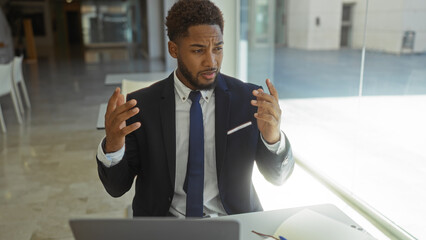 Handsome young man in a business suit gesturing passionately while working on a laptop in a modern...