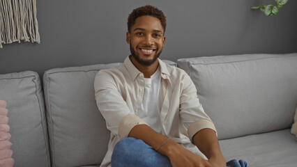 Fototapeta premium Handsome young man sitting comfortably in a modern living room with light gray sofa and minimalist decor