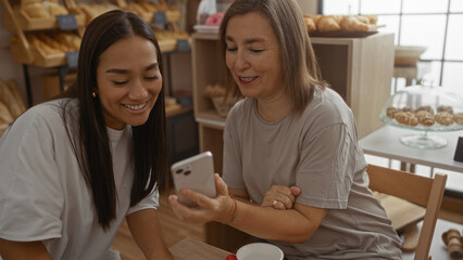 Woman and daughter sharing a moment of love, looking at a phone together in a cozy bakery shop