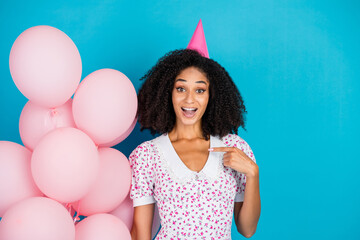 Fototapeta premium Cheerful Young Woman Celebrating in a Party Hat With Balloons, Wearing a Trendy Floral Dress Against a Vibrant Blue Background