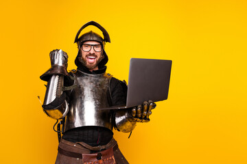 Knight in medieval armor excitedly using a laptop against a yellow background