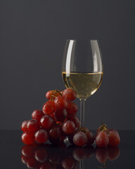 Elegant presentation of white wine alongside fresh red grapes on a dark background