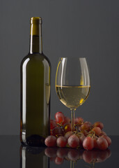 Obraz premium Elegant presentation of gray wine bottle and glass with grapes on a reflecting surface