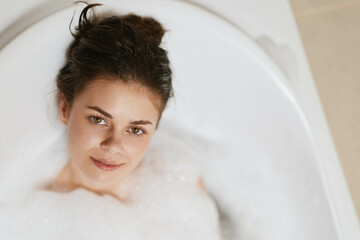 Calm young woman relaxing in a bubble bath, enjoying a moment of self-care and tranquility. Spa and wellness concept with soft lighting in the background.