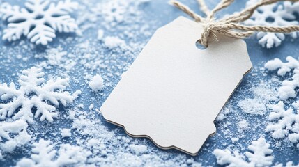 Blank gift tag lying on snowy blue background with snowflakes decoration for christmas or winter holidays