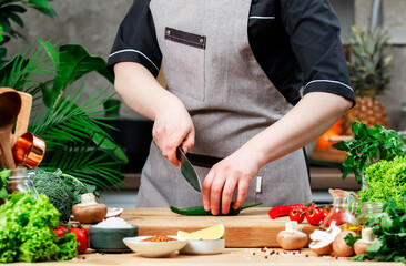 Chef food blogger cuts hot green chili pepper. Cozy kitchen with wooden table, kitchenware, vegetables, herbs and ingredients for cooking. Healthy vegan eating, culinary, recipes, blogging