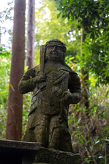 Obraz premium Stone statue of a warrior surrounded by lush greenery in a tranquil forest setting