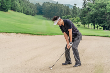 バンカーショットを打つ男性ゴルファー
