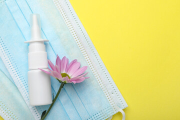 Allergy treatment. Nasal spray, protective masks and flower on yellow background, top view. Space for text