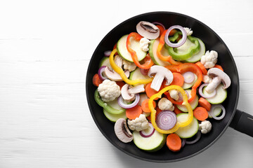 Frying pan with mix of vegetables and mushrooms on white wooden table, top view. Space for text
