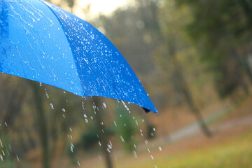Open blue umbrella under pouring rain outdoors, closeup. Space for text