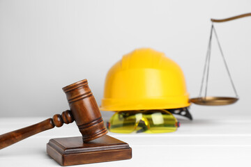 Accident at work concept. Gavel, scales and construction worker's protective gear on white wooden table, selective focus