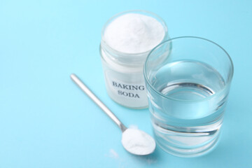 Glass of water and baking soda on light blue background, selective focus. Space for text