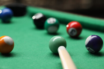 Many colorful billiard balls and cue on green table indoors, closeup