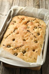 Delicious focaccia bread with olives and thyme in baking dish on wooden table, closeup