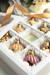 Box with tasty chocolate candies in shape of baubles and Christmas decor on white background, closeup