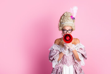 Young woman in historical costume with wig and megaphone in front of pink background portraying noble and playful character