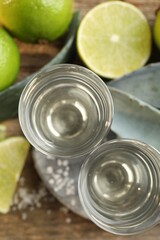 Tequila shots with salt, limes and agave leaves on wooden table, flat lay