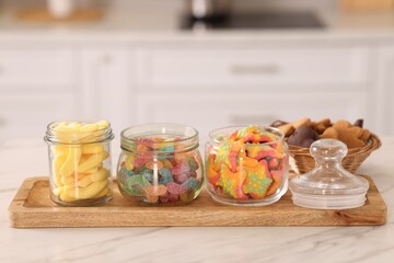Tasty gummy candies and cookies on white marble table