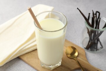 Delicious vanilla milk in glass, pods and spoon on grey table, closeup